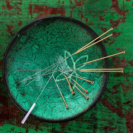 green ceramic Asian Bowl with needles for acupuncture on an old green paint wooden board